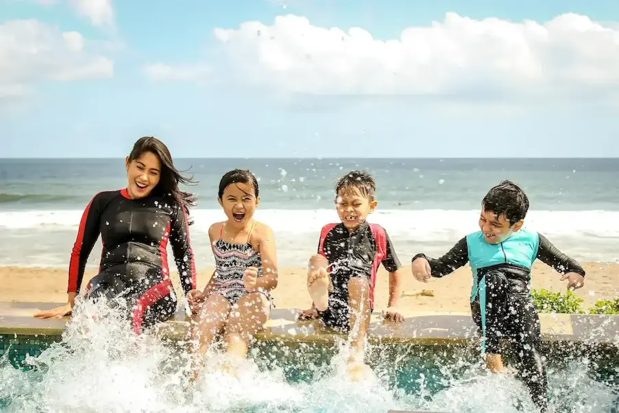 Family splashing water at beachside pool on sunny day, enjoying fun and laughter together.