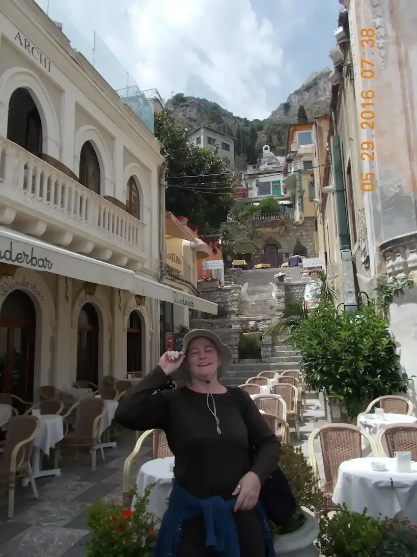 Woman smiling in a charming outdoor cafe with scenic hillside view in Positano, Italy, on a sunny day.