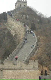 People walking up a steep section of the Great Wall of China on a cloudy day.