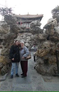 Two people pose by rocky formations at a historical site with a traditional building in the background.
