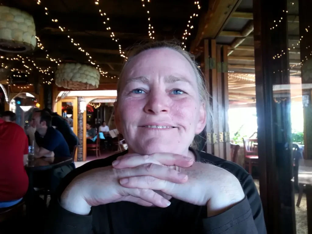 Person smiling in a cozy restaurant with warm lighting and festive décor in the background.