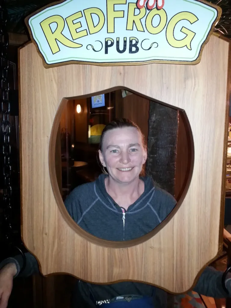Woman smiling inside a wooden frame at RedFrog Pub entrance. Fun atmosphere.
