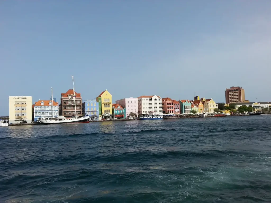 Colorful waterfront buildings in Willemstad, Curaçao under clear blue sky, viewed from the ocean.