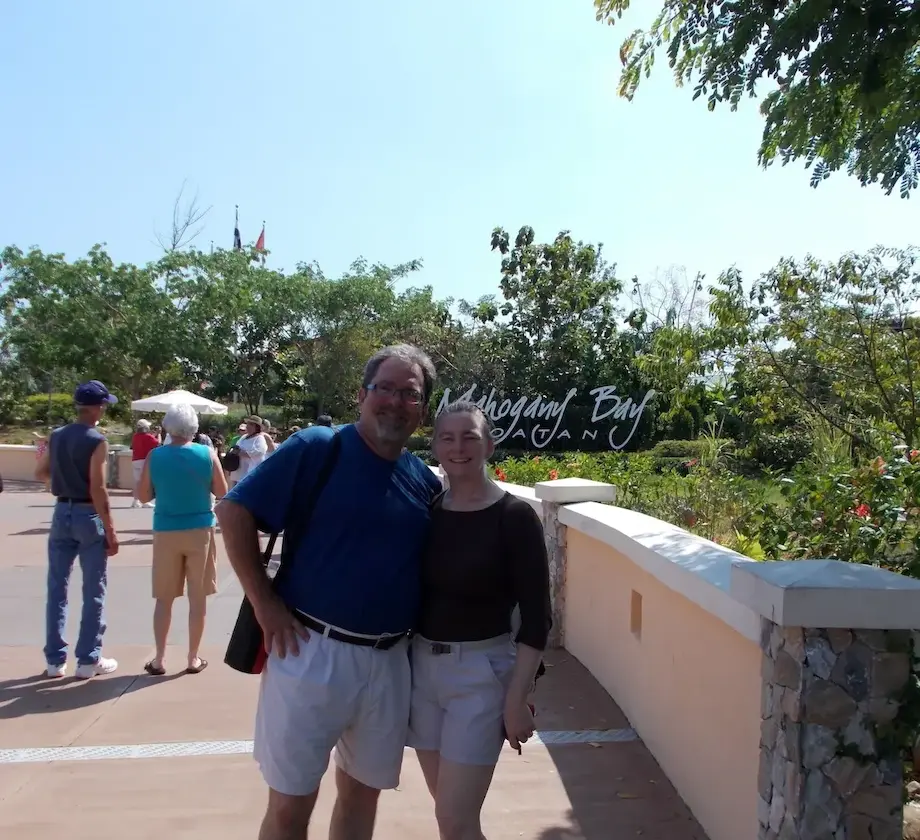 Couple posing at Mahogany Bay Roatan, surrounded by greenery and tourists on a sunny day.