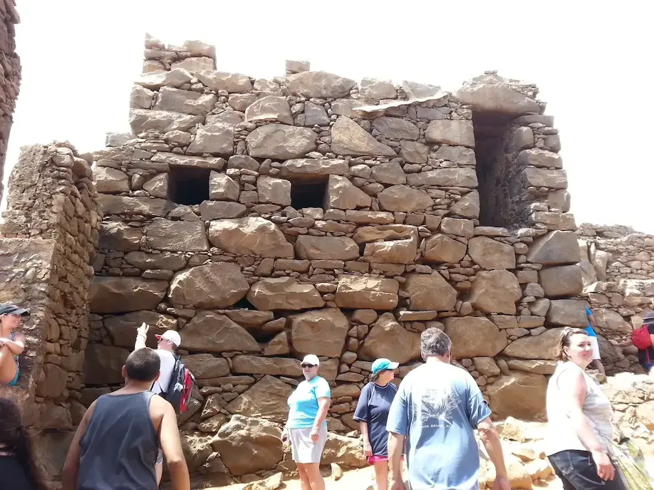 Visitors explore ancient stone ruins in a sunny, historical site.