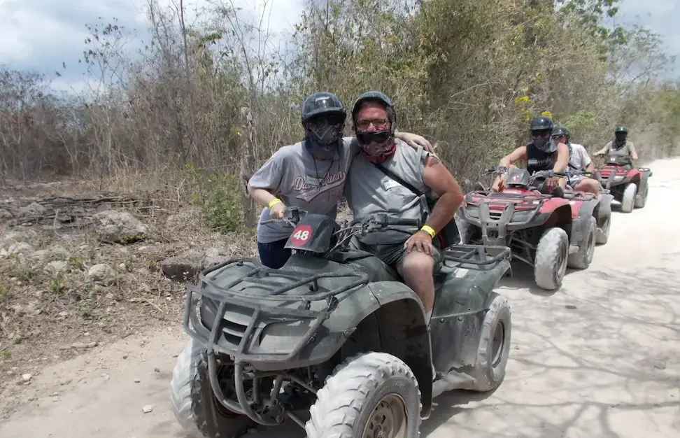 Group enjoying an ATV adventure on a dusty trail in the wilderness, wearing helmets and protective gear.