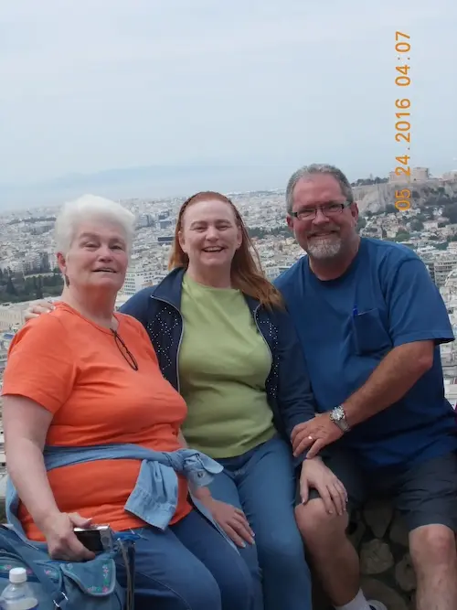 Three people smiling with a city view in the background, enjoying a day outdoors.