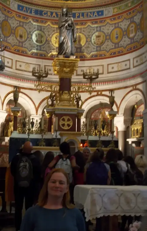 Interior of a richly decorated church with visitors and a statue on an ornate altar in the background.