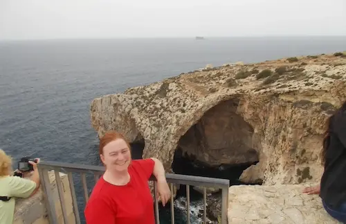 Woman at Blue Grotto in Malta, smiling by the seaside cliffs with ocean view in background.