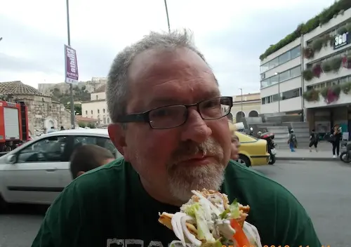 Man enjoying a loaded sandwich outdoors in a city street scene.