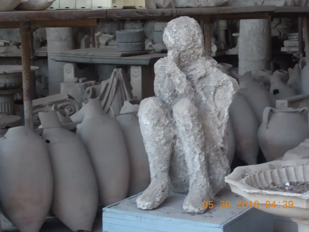 Statue of a seated figure in an archaeological site surrounded by ancient pottery.