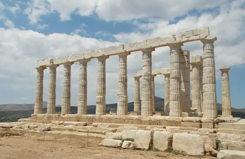 Ancient Greek temple ruins with tall columns under a blue sky and scattered clouds.