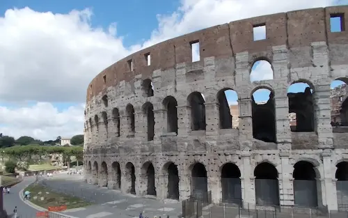 Exterior view of the Colosseum in Rome under a blue sky, showcasing ancient architecture and historical significance.